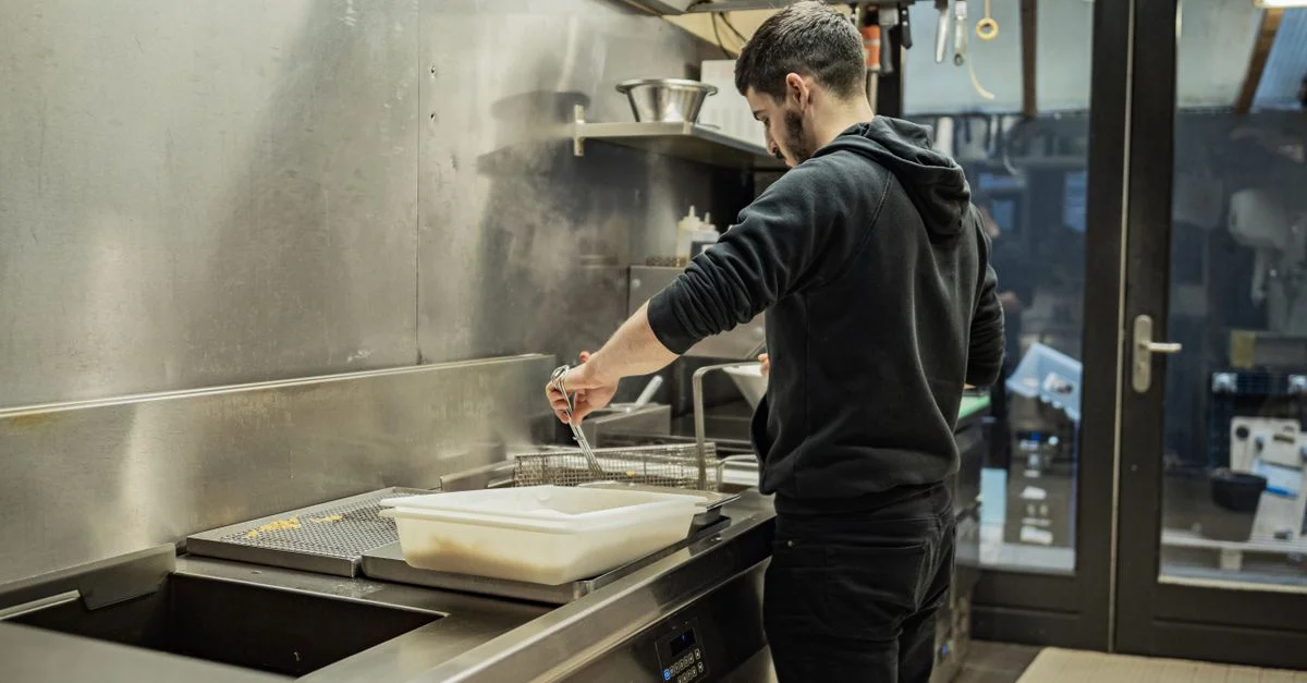 Un chef en veste noire cuisine dans une cuisine moderne en acier inoxydable, en faisant frémir des aliments à l'intérieur.