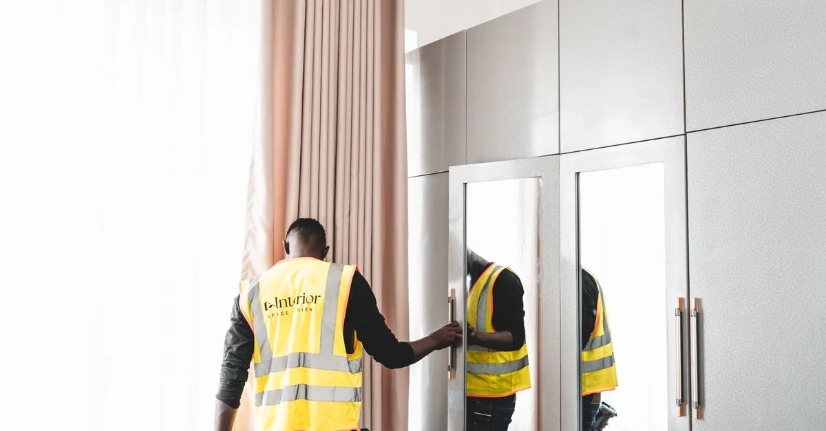 Un technicien de maintenance en gilet de sécurité examine un miroir de garde-robe à l'intérieur.