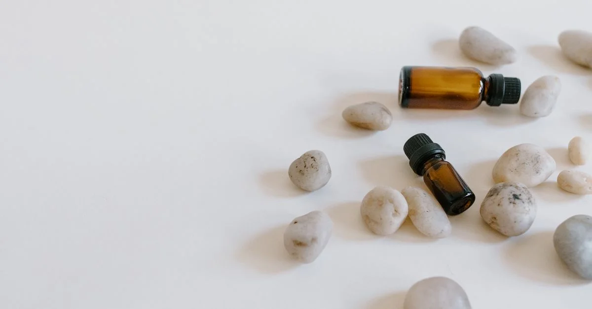 Arrangement minimaliste de bouteilles d'huiles essentielles entourées de pierres sur un fond clair.