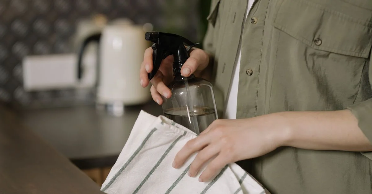 Une personne nettoyant un plan de travail de cuisine avec un spray et un chiffon, maintenant la propreté.