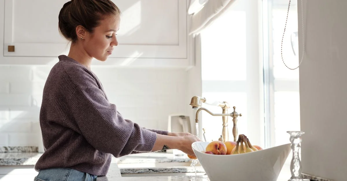 Une femme lave des fruits dans une cuisine moderne et lumineuse, mettant en avant un mode de vie sain.