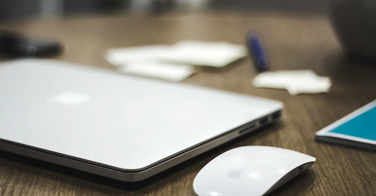 Un espace de travail propre et minimaliste avec un ordinateur portable fermé et une souris sans fil sur un bureau en bois.