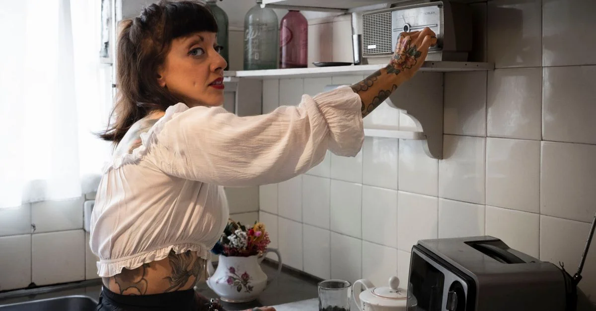 Une femme tatouée dans une cuisine vintage allume une radio, créant une ambiance rétro.