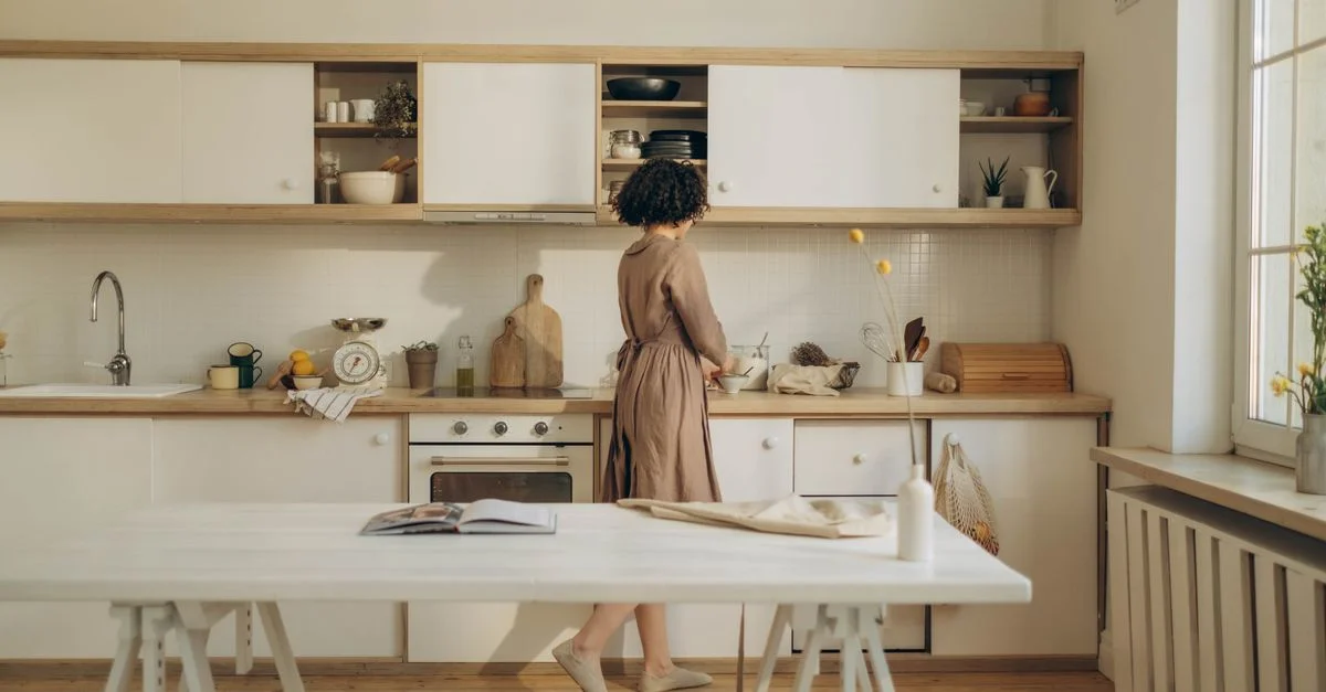 Une femme cuisinant de manière décontractée dans une cuisine minimaliste baignée de lumière naturelle.