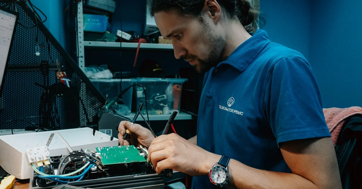 Technicien travaillant sur une carte de circuit imprimé dans un atelier bien équipé, faisant preuve de compétences techniques et de précision.