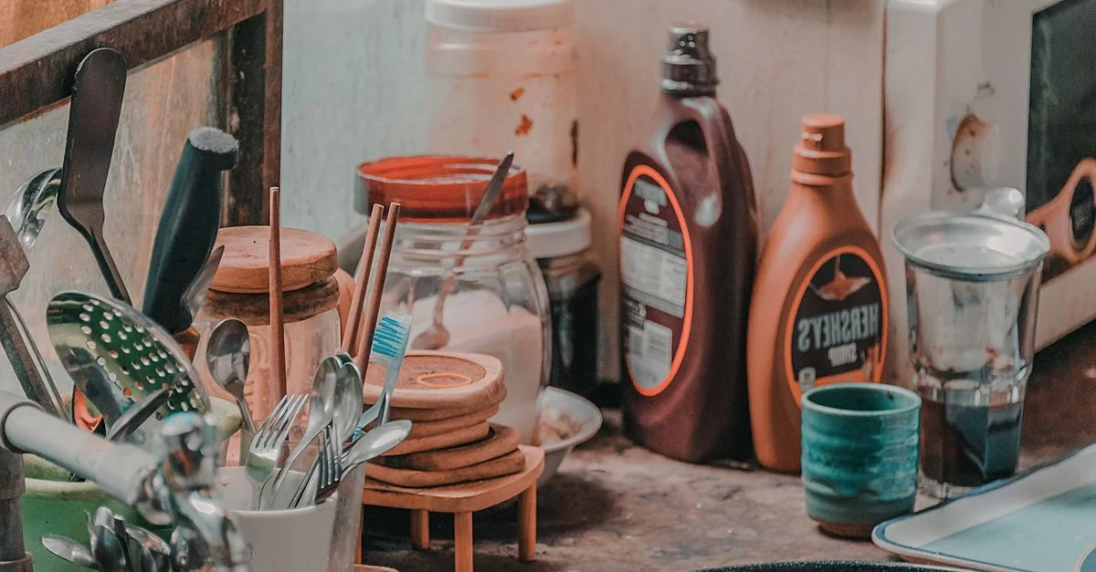 Un plan de travail de cuisine encombré rempli d'ustensiles, de bocaux et de condiments, créant une ambiance rustique et accueillante.