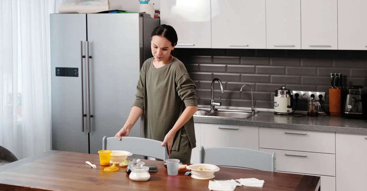 Une femme rangeant la cuisine, organisant la vaisselle et nettoyant la table dans un environnement familial chaleureux.