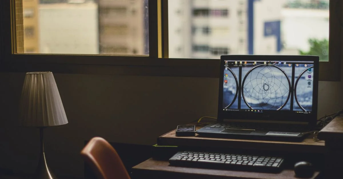 Un bureau à domicile paisible avec un ordinateur portable, une lampe et une vue sur la ville à travers la fenêtre.