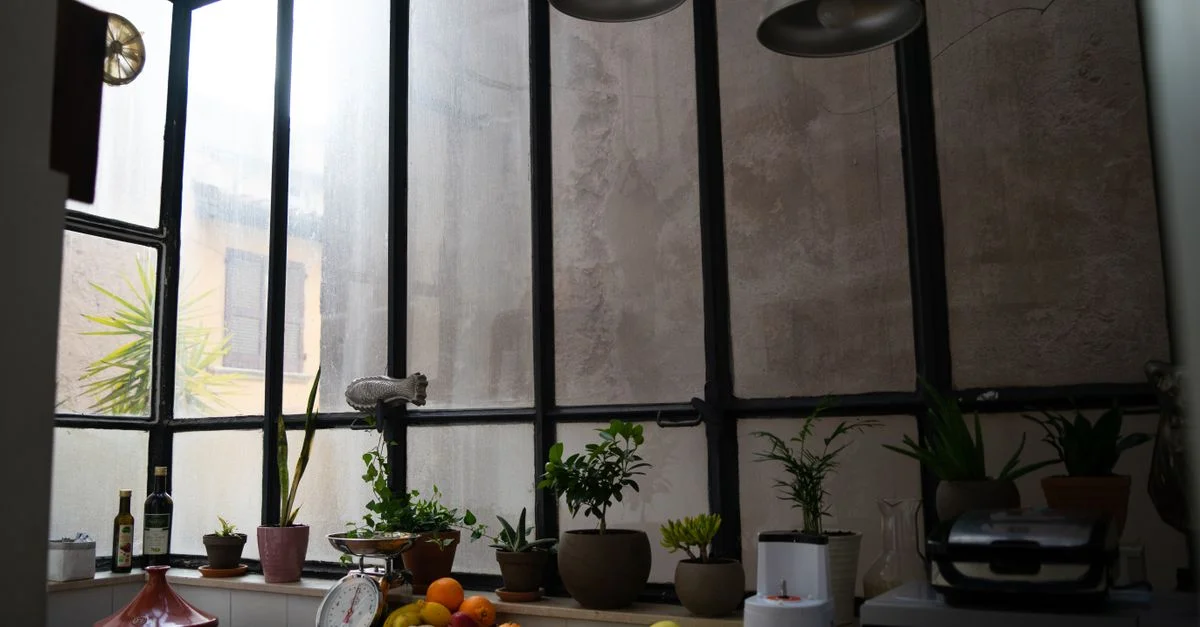 Un cadre de cuisine cosy avec des fruits et des plantes sur une table en bois, éclairé par de grandes lampes industrielles.