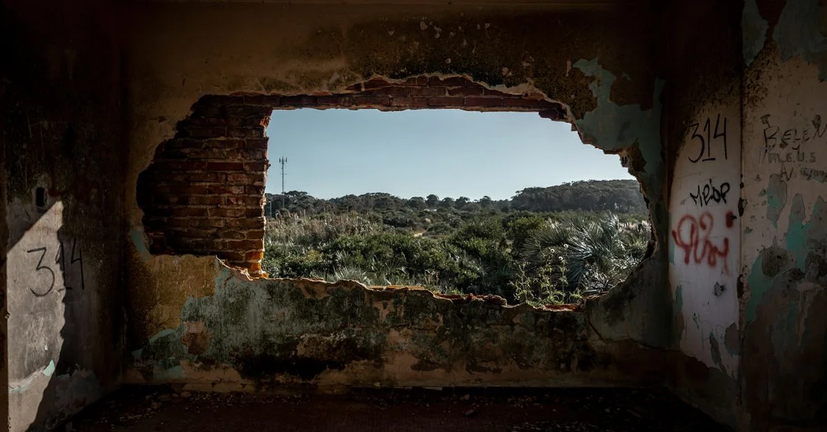 Un paysage rustique vu à travers un trou dans un bâtiment abandonné et vandalisé.
