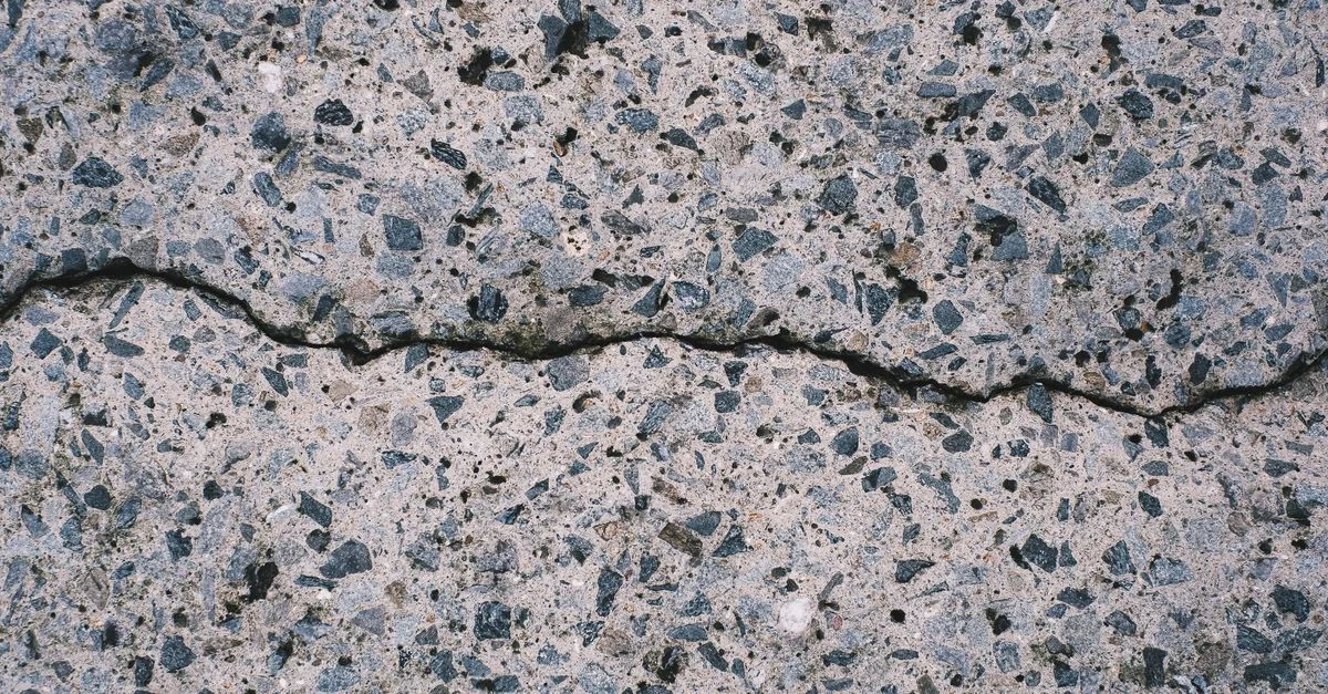 Vue détaillée d'une surface en béton texturé avec agrégats et fissures visibles.