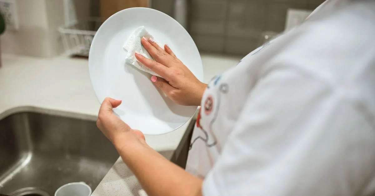 Une personne nettoyant une assiette en céramique à la main dans une cuisine moderne.