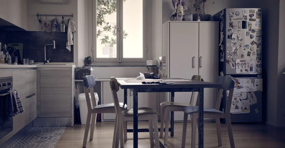Une cuisine lumineuse et minimaliste avec une table et des chaises vintage, éclairée par la lumière naturelle d'une fenêtre.