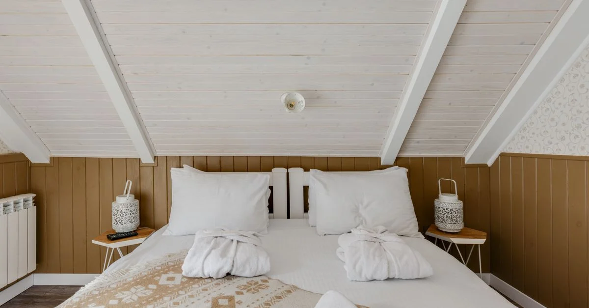 Chambre sous les combles accueillante avec linge de lit et peignoirs sur un lit blanc, parfait pour se détendre.