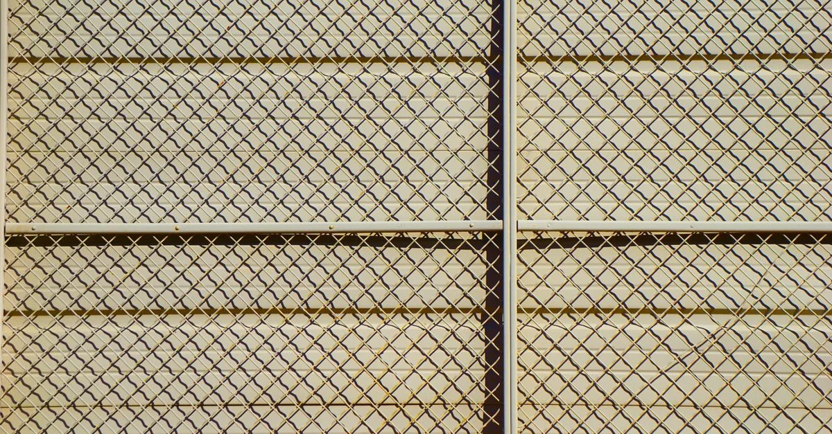 Motif détaillé d'une clôture en grillage projetant des ombres et créant un effet de grille texturée.