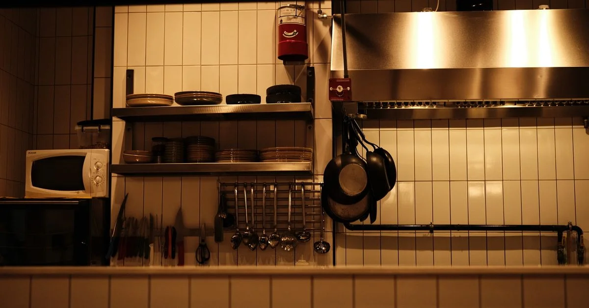Une cuisine de restaurant bien organisée avec des ustensiles, des poêles et un four à micro-ondes.