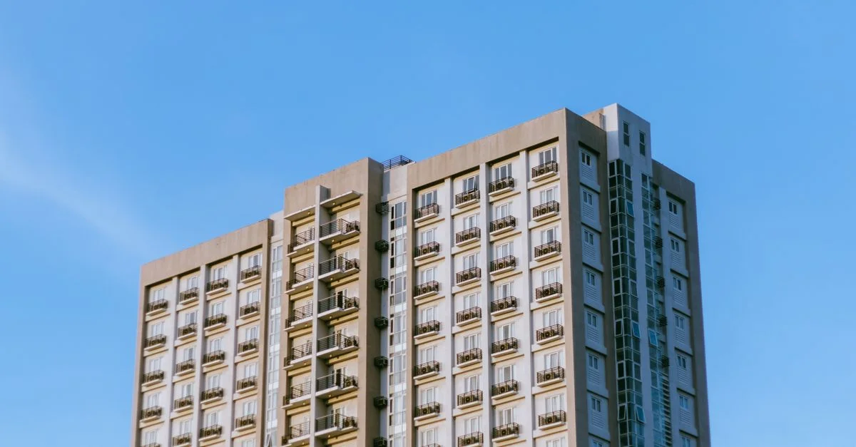 Immeuble d'appartements contemporain en hauteur avec balcons sous un ciel bleu clair.
