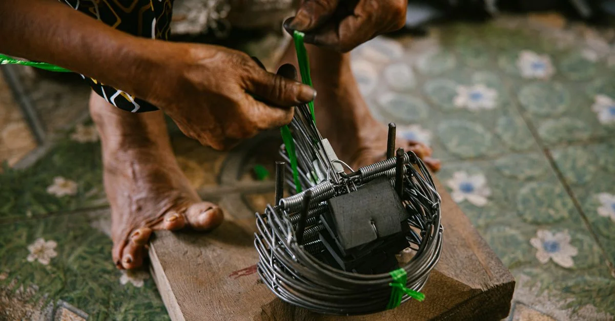 Mains d'artisan tissant habilement un piège en métal sur une base en bois à l'intérieur. Artisanat traditionnel.
