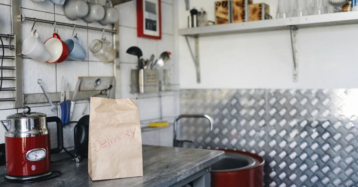 Un cadre de cuisine domestique avec un sac de livraison en papier sur le comptoir, entouré d'ustensiles de cuisine et d'appareils.