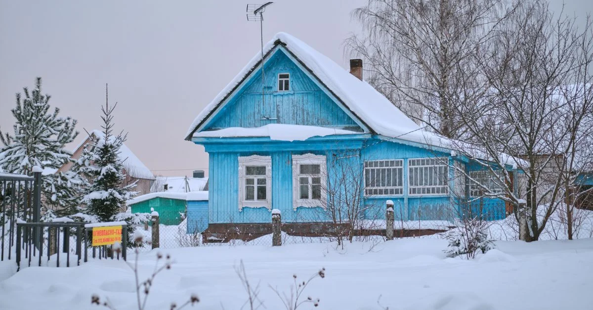 Charmante maison en bois bleue entourée de neige dans un cadre de village hivernal tranquille.
