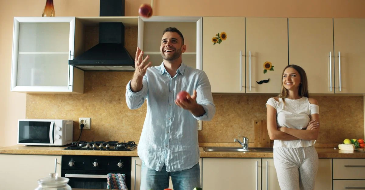 Un couple joyeux s'amuse à jongler avec des pommes dans une cuisine moderne et lumineuse.