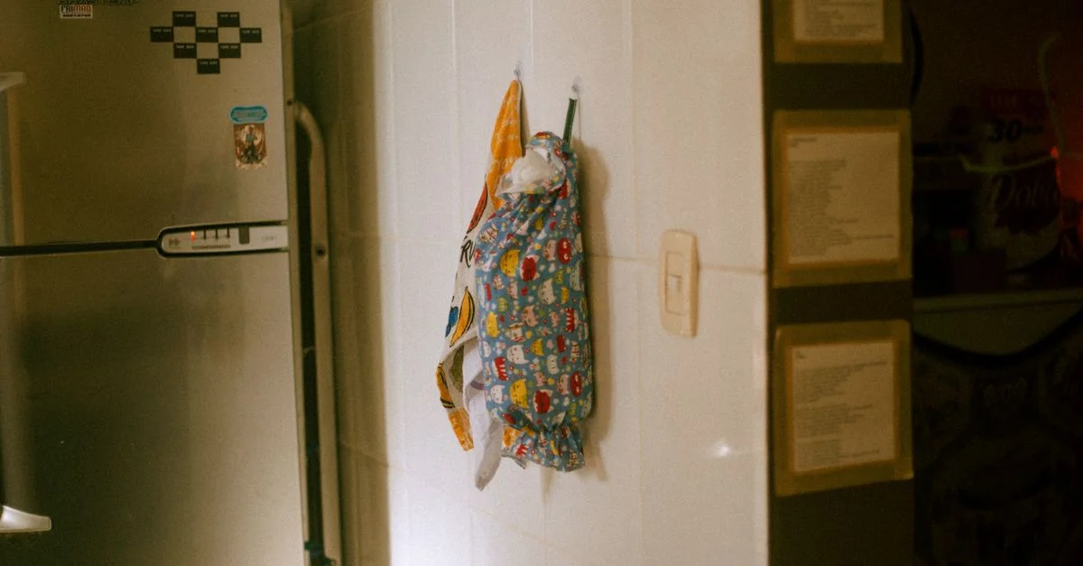 Une scène de cuisine domestique montrant un tablier décoré suspendu à côté d'un réfrigérateur en acier inoxydable.