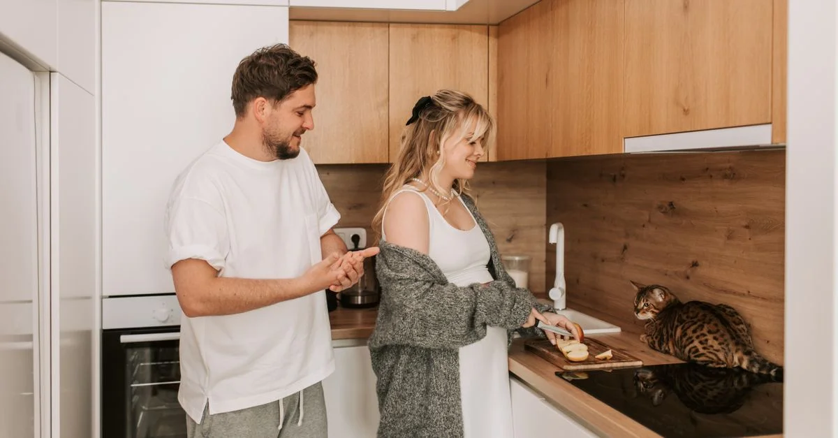 Un couple cuisinant ensemble dans une cuisine moderne, avec leur chat qui regarde. Parfait pour les thèmes de style de vie et de maison.