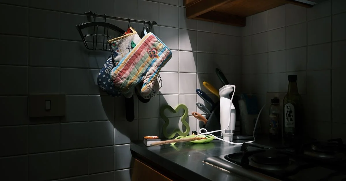 Un coin de cuisine faiblement éclairé avec des ustensiles de cuisine et des gants de four sur le plan de travail.