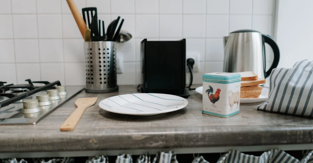 Un plan de travail de cuisine propre avec des ustensiles, une bouilloire et une boîte en fer au design vibrant.